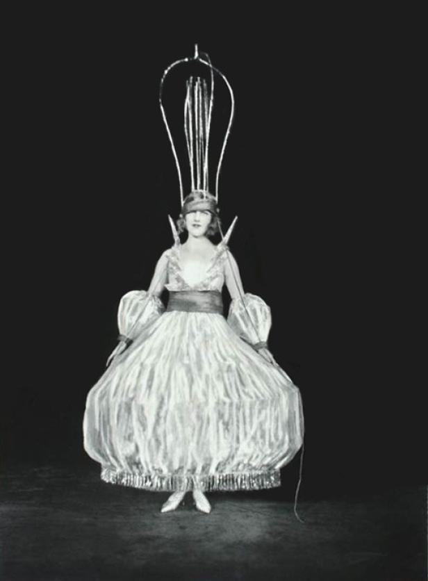 Eine Frau in einem extravaganten Kostüm mit einem hohen, drahtartigen Kopfschmuck.