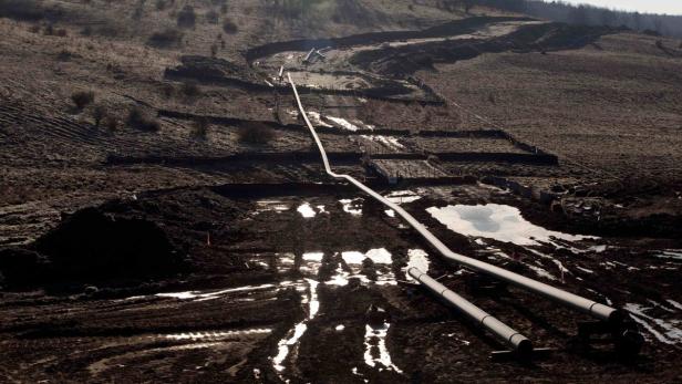 Eine Pipeline verläuft durch eine hügelige, schlammige Landschaft.