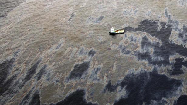 Ein kleines Boot fährt durch eine große Ölverschmutzung auf dem Meer.