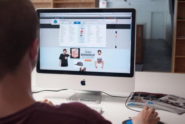 Ein Mann sitzt vor einem iMac und betrachtet eine Webseite mit Modeartikeln.