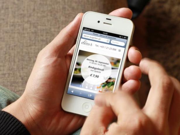 Eine Person hält ein iPhone in der Hand und betrachtet die Webseite von „decor-augarten.at“.