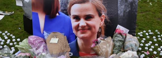 Ein Porträt von Jo Cox, umgeben von Blumen und Kerzen auf einer Wiese.