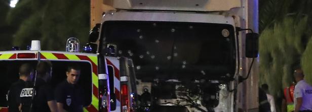 Die Windschutzscheibe eines Lastwagens ist mit zahlreichen Einschusslöchern übersät; Polizisten stehen daneben.