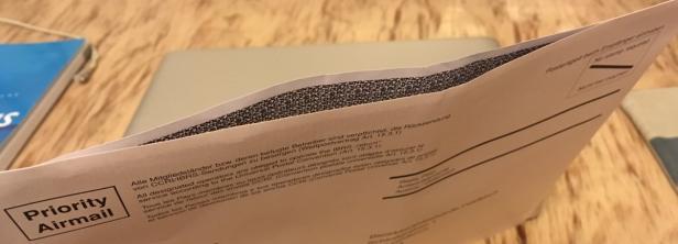 Ein geöffneter Briefumschlag mit der Aufschrift „Priority Airmail“ liegt auf einem Tisch.