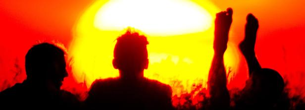 Silhouetten von drei Personen vor einem hellen, roten und gelben Hintergrund.