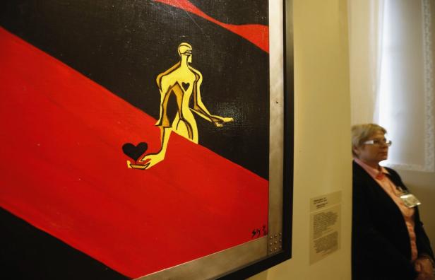 Ein Gemälde mit einer goldenen Figur, die ein schwarzes Herz in der Hand hält, vor einem rot-schwarzen Hintergrund.