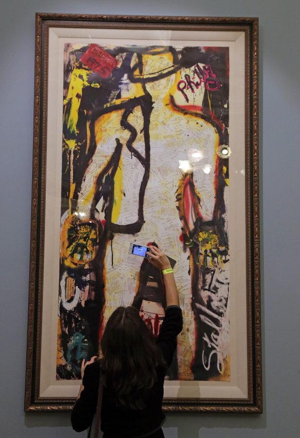 Eine Frau fotografiert ein großes, gerahmtes abstraktes Gemälde.