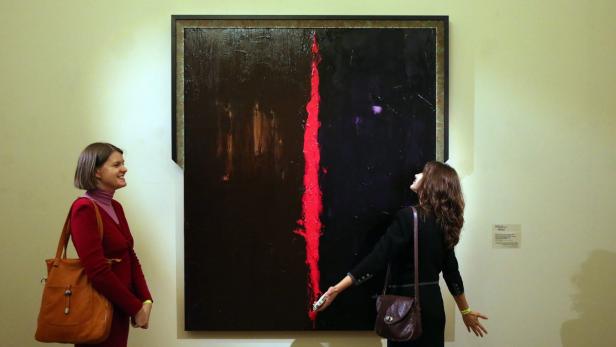 Zwei Frauen betrachten ein abstraktes Gemälde mit einem roten Streifen in einer Kunstgalerie.