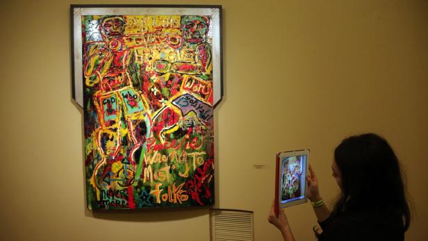 Eine Frau fotografiert ein farbenfrohes Gemälde in einer Kunstgalerie mit einem Tablet.