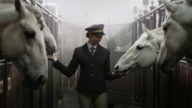 Eine Frau in Uniform füttert weiße Pferde in einem Stall.