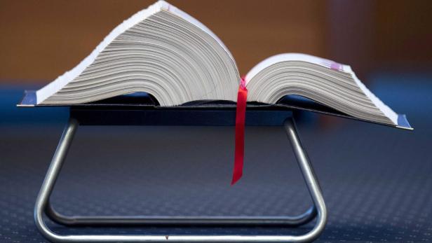 Ein aufgeschlagenes Buch mit einem roten Lesezeichen liegt auf einem Ständer.