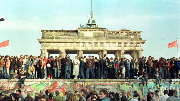 Menschen stehen auf der Berliner Mauer vor dem Brandenburger Tor.