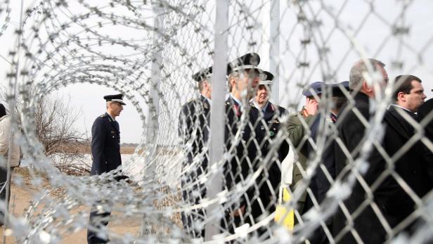 Militärpersonal steht hinter einem Stacheldrahtzaun.