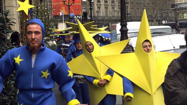 Eine Gruppe von Menschen in Sternenkostümen und blauen Anzügen mit gelben Sternen läuft durch eine Stadt.