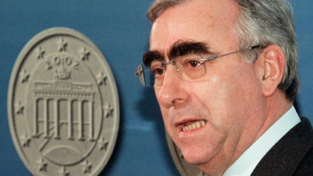 Ein Mann mit Brille und markanten Augenbrauen vor einem Abzeichen mit dem Brandenburger Tor.