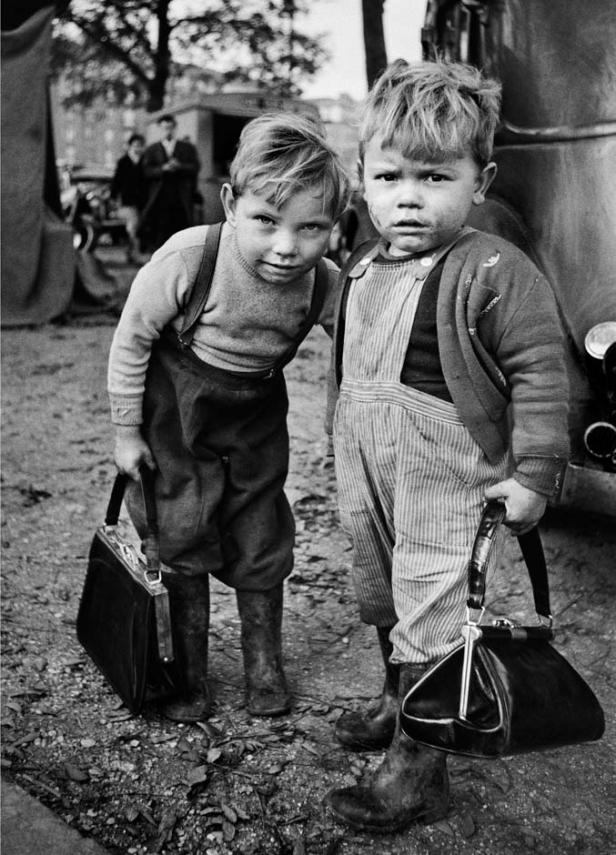 Zwei kleine Jungen in Overalls halten Handtaschen in der Hand.