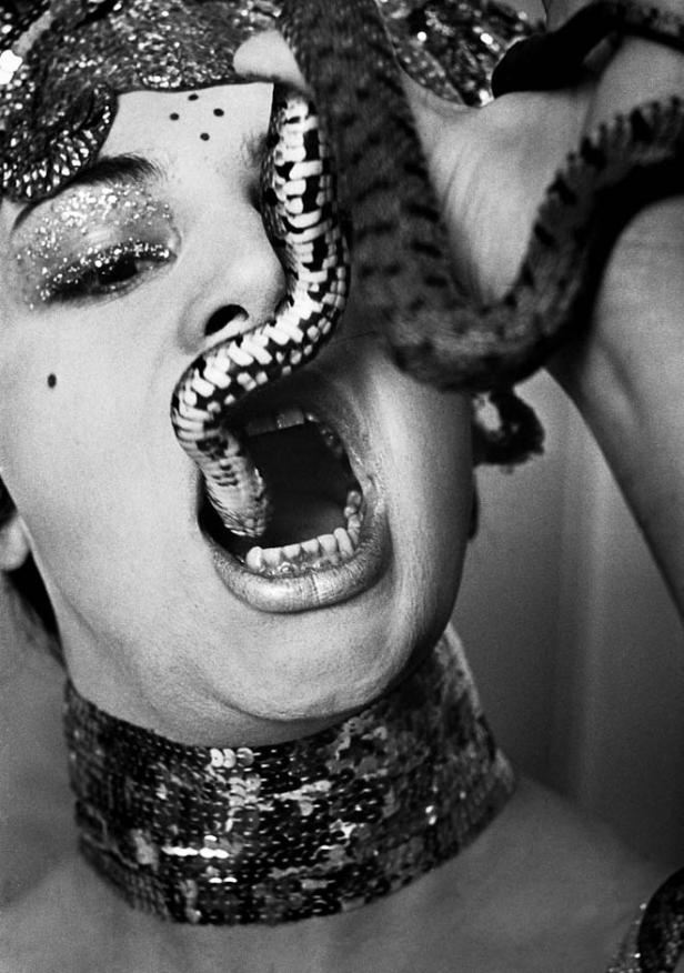 Eine Frau mit Glitzer-Make-up hat eine Schlange im Mund.