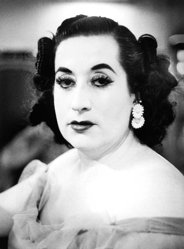 Schwarzweißporträt einer Frau mit starkem Make-up und Blumenohrringen.
