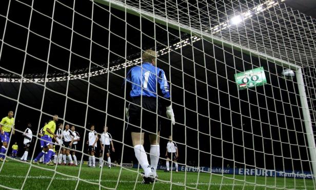 Ein Fußballtorwart steht vor dem Netz, während ein Fußballspiel stattfindet.