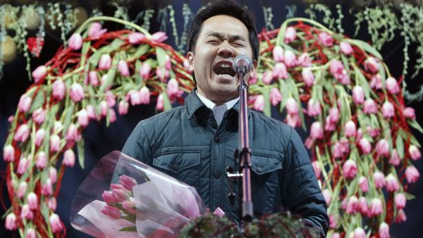Ein Mann singt mit einem Blumenstrauß in der Hand vor einem Mikrofon.