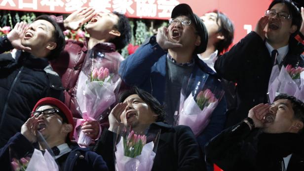 Eine Gruppe japanischer Männer jubelt mit Blumensträußen in der Hand.