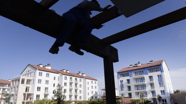 Ein Bauarbeiter arbeitet an einer Holzkonstruktion vor dem Hintergrund von Apartmentgebäuden.
