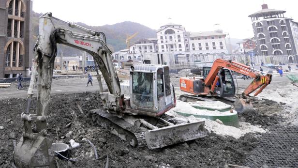Zwei Bagger stehen auf einer Baustelle vor Gebäuden.