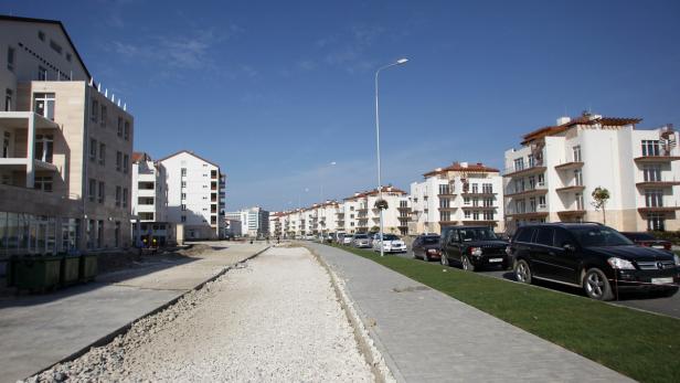 Eine Straße mit geparkten Autos und weißen Gebäuden an einem sonnigen Tag.