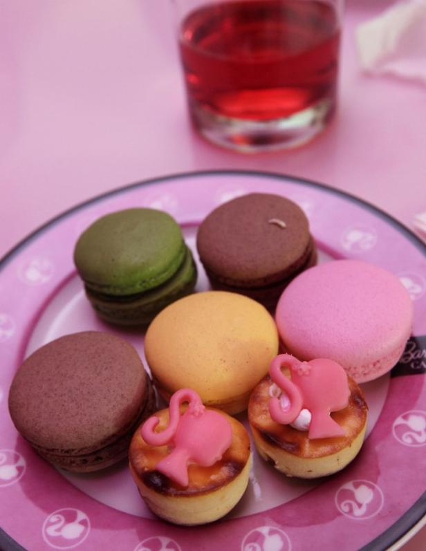 Auf einem Teller liegen bunte Macarons und kleine Küchlein mit Barbie-Dekoration.