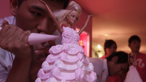 Ein Konditor verziert einen Kuchen in Form eines rosa Kleides mit einer Barbie-Puppe darauf.