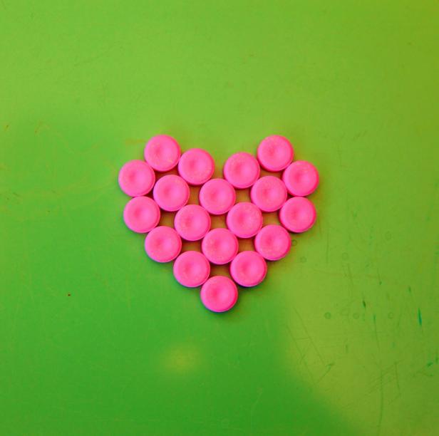 Rosa Pillen sind in Herzform auf einem grünen Hintergrund angeordnet.
