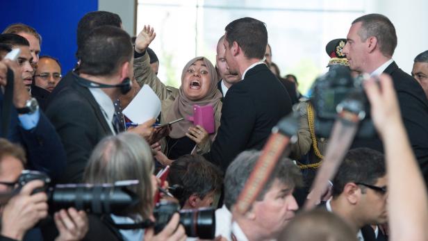 Eine aufgeregte Frau mit Hidschab inmitten einer Menschenmenge aus Fotografen und Sicherheitsleuten.