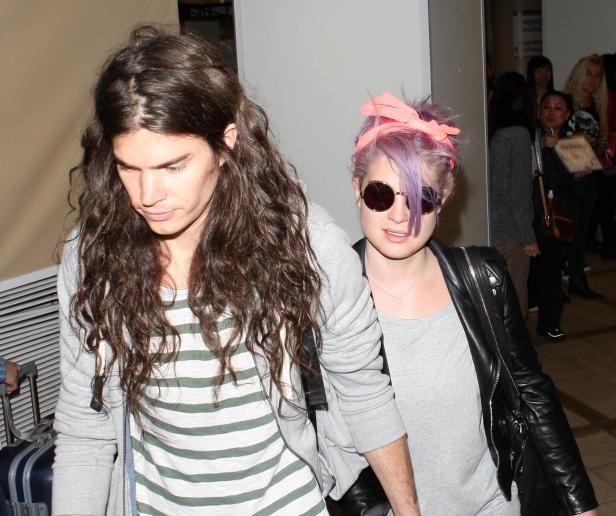 Kelly Osbourne mit lila Haaren und ein Mann mit langen, braunen Haaren gehen zusammen.