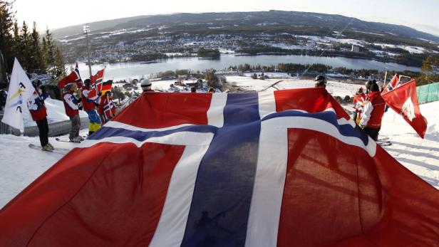 Skifahrer halten eine große norwegische Flagge auf einem schneebedeckten Hügel.