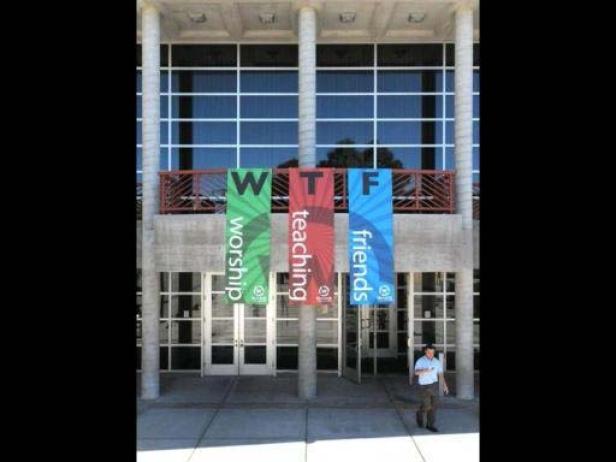 Ein Mann geht vor einem Gebäude mit Bannern, die „WTF“ und „Worship Teaching Friends“ zeigen.