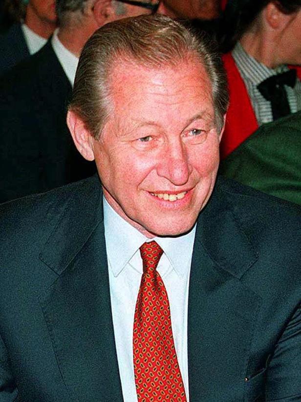 Ein lächelnder Mann mit Anzug und roter Krawatte.