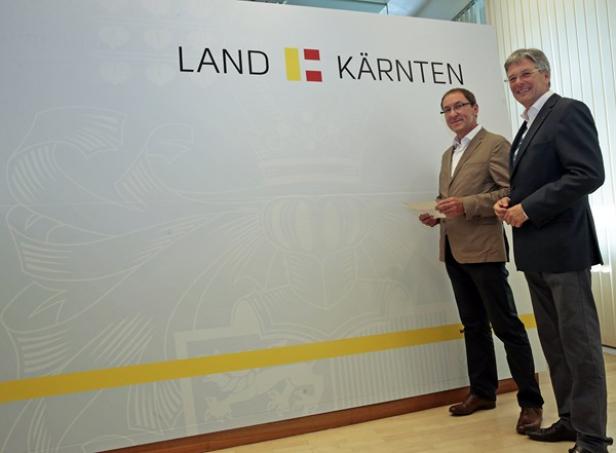 Zwei Männer stehen vor einem Banner mit der Aufschrift „Land Kärnten“.