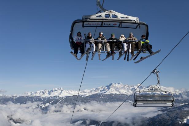 Eine Gruppe Skifahrer sitzt in einem Sessellift mit Blick auf schneebedeckte Berge.