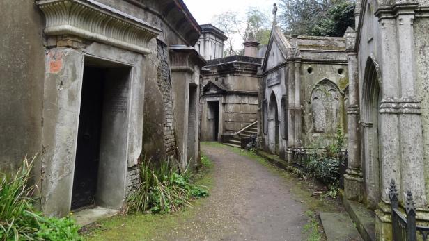 Ein Weg führt durch einen alten Friedhof mit steinernen Mausoleen.