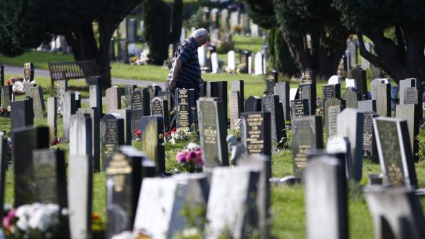 Ein Mann steht auf einem Friedhof zwischen vielen Grabsteinen.