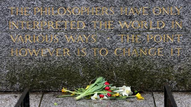 Ein Denkmal mit einem Zitat und einem Blumenstrauß davor.