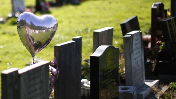 Ein silberner Herzluftballon schwebt über einem Grabstein auf einem Friedhof.