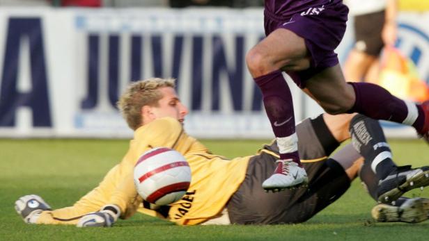 Ein Fußballtorwart liegt auf dem Rasen, während ein anderer Spieler über ihn springt.