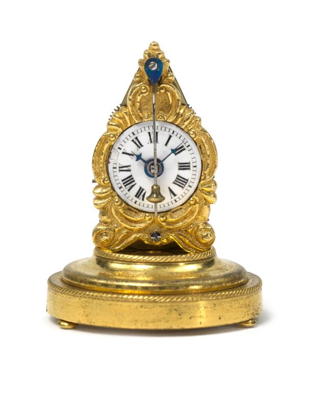 Eine verzierte goldene Tischuhr mit römischen Ziffern auf weißem Hintergrund.