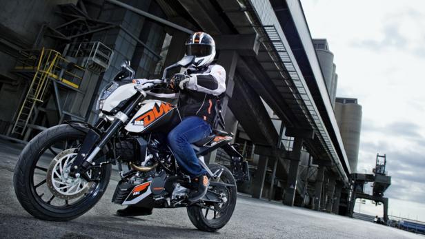 Ein Motorradfahrer auf einer KTM 125 Duke vor einem Industriegebäude.