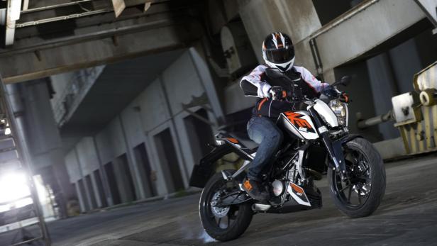 Ein Motorradfahrer mit Helm fährt auf einer KTM durch eine Industriehalle.