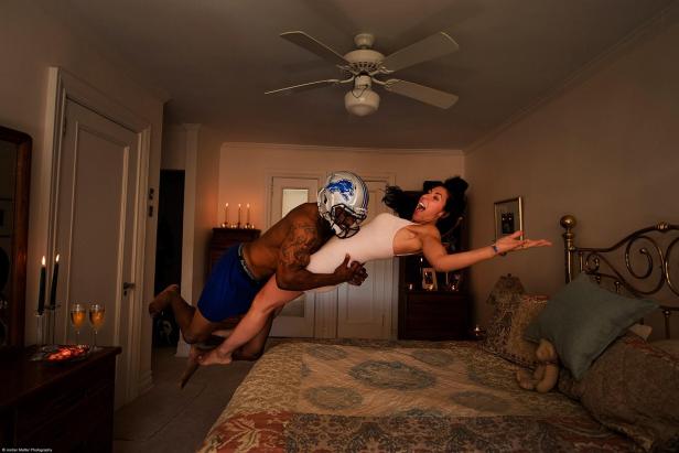 Ein Mann mit Footballhelm trägt eine Frau im Schlafzimmer.