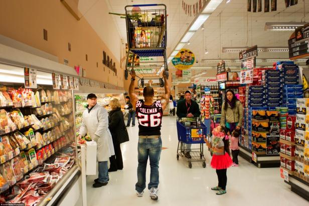 Ein Mann stemmt im Supermarkt zwei volle Einkaufswagen über seinem Kopf.