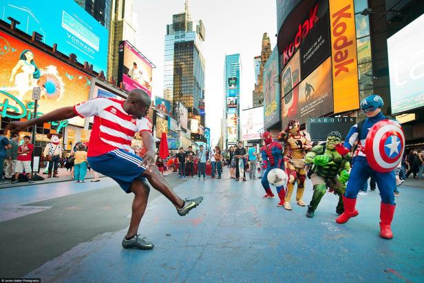 Ein Mann spielt Fußball mit als Superhelden verkleideten Personen am Times Square in New York.