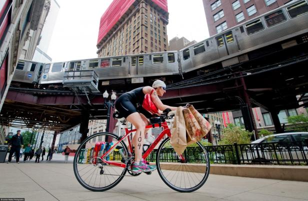 Eine Radfahrerin mit Startnummer fährt unter einer Hochbahn in einer Stadt hindurch.
